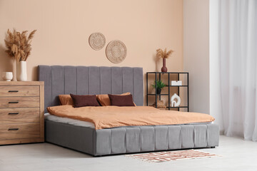 Stylish bedroom with comfortable bed, chest of drawers and vase of pampas grass