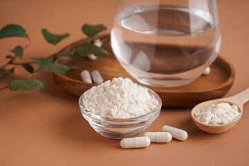 Glass of water, bowl and spoon with collagen powder on brown background