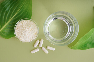 Bowl with collagen powder, pills and glass of water on green background