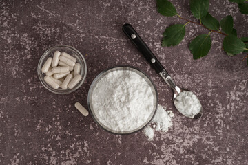 Glass, bowl and spoon of collagen powder with pills on grey grunge background