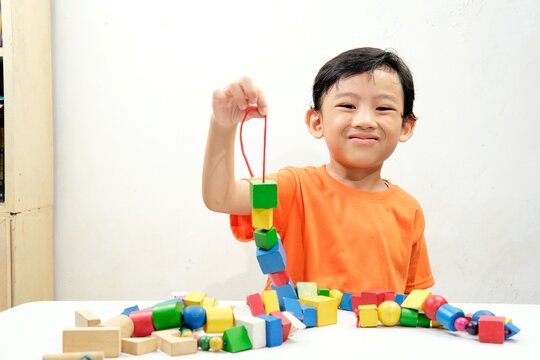 A young boy intently threads colorful wooden beads, developing fine motor skills and creativity. Perfect for educational content on child development, learning, and fun activities.