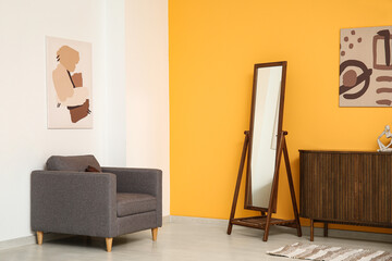 Armchair, chest of drawers, houseplant and mirror on yellow wall in room