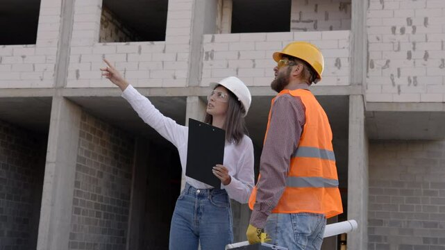 Female architect pointing at something while discussing with construction worker at building site