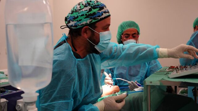 Dentist operating the dental equipment for a dental implant, serum bag in foreground