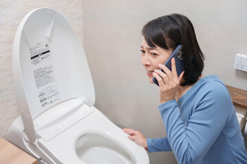 トイレのトラブルで水道業者に電話する女性