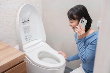 トイレのトラブルで水道業者に電話する女性