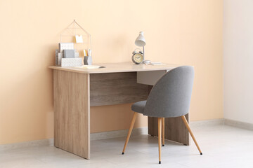 Stylish workplace with lamp and armchair near beige wall in office