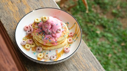 Delicious waffles topped with two scoops of pink ice cream, colorful sprinkles, and cereal pieces, served in a white bowl. A tempting dessert showcasing sweetness and texture for a delightful treat.