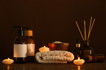 Glowing candles with spa cosmetics, towel and sea salt on dark background
