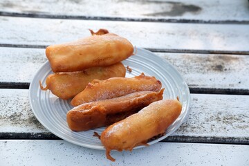Close-up of golden crispy pisang goreng or banana fritters dusted with powdered sugar,served on a...