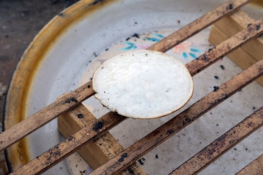 serabi pancakes rest on wooden sticks,freshly cooked over traditional wood fire.The rustic setting and simple tools emphasize the authentic, traditional method of preparing Indonesian delicacy