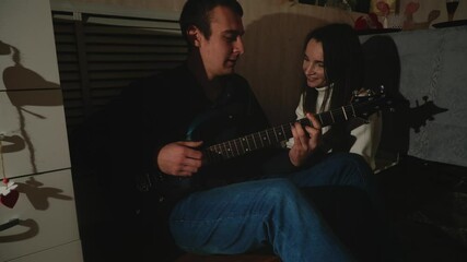 Valentines day concept. Happy couple in love indoors. A young man plays the guitar for his beloved