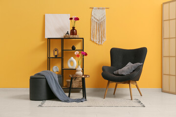 Armchair, pouf and gerbera flowers in vase on coffee table in interior of living room