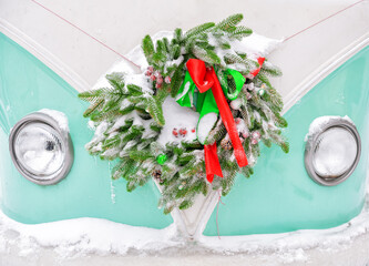 Festive Christmas wreath with ribbons decorates a retro van in snowy winter