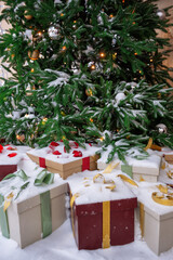 Snow-covered Christmas tree with glittering ornaments, festive lights and gift boxes wrapped in ribbons