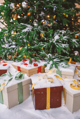 Snow-covered Christmas tree with glittering ornaments, festive lights and gift boxes wrapped in ribbons