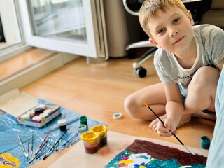 cute little boy drawing a picture with gouache paint on the floor at home