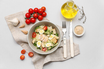 Bowl of tasty chicken Caesar salad with tomatoes, garlic and bowl of sauce on grey background