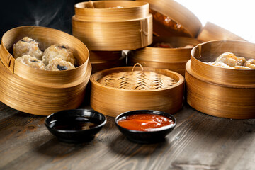 Assorted Chinese dim sum dumplings on the wooden basket bowl with sauce and soy sauce on the wooden table