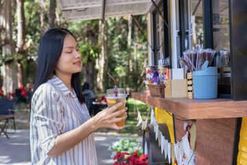Young Asian woman enjoying the outdoor atmosphere reached out and picked up a clear plastic cup of a cold drink. along with ice cubes Indicates iced tea or refreshing fruit juice.