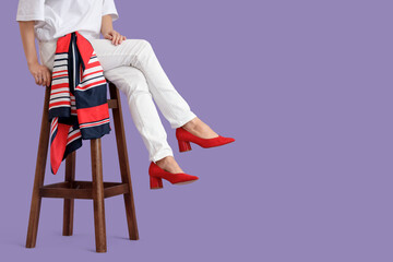 Woman in red heels sitting on stool against lilac background