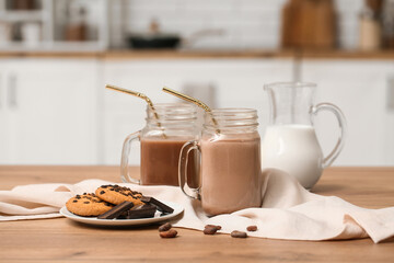 Mason jars of sweet chocolate milk and plate with tasty cookies on wooden table in kitchen