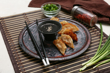 Plate of fried Japanese gyoza with bowl of soy sauce and green onion on white background, closeup