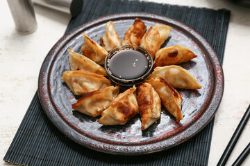 Plate with fried Japanese gyoza and bowl of soy sauce on white background