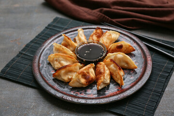 Plate with fried Japanese gyoza and bowl of soy sauce on black background, closeup