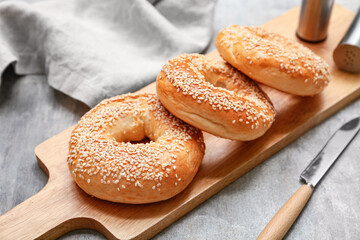 Wooden board of tasty bagels with sesame seeds on grey background, closeup