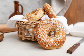 Wicker bowl of tasty bagels with sesame seeds on white background