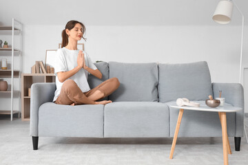 Obraz premium Young woman meditating on sofa at home