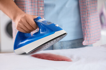 Handsome young man with iron and burned t-shirt on board at home, closeup