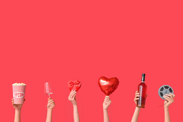 Female hands with bucket of popcorn, wine glass, air balloon in shape of heart, film reel, bottle of wine and gift box on red background. Valentine's Day celebration
