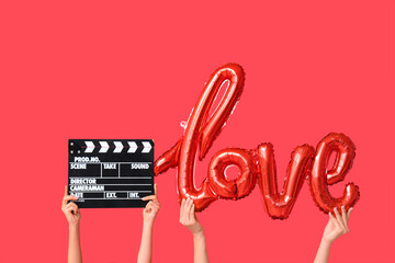 Female hands with air balloon in shape of word LOVE and movie clapper on red background....