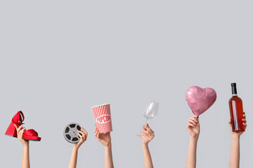 Female hands with bucket of popcorn, heeled shoe, film reel, bottle of wine, glass and air balloon in shape of heart on white background. Valentine's Day celebration
