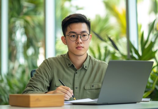Young man with glasses working on laptop in calm green environment