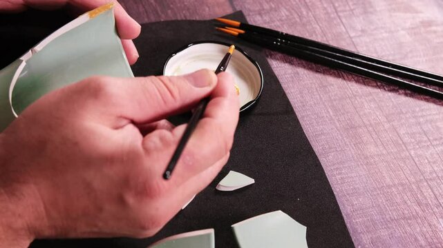 Kintsugi concept. Person repairing a cup with gold.