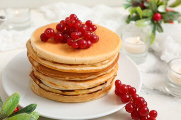 Plate of sweet pancakes with red currants, burning candles and mistletoe branches on white background
