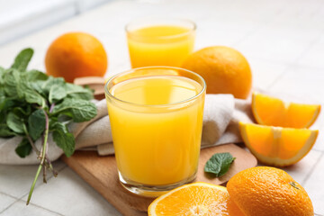 Glasses of tasty juice with oranges and mint leaves on white tile background