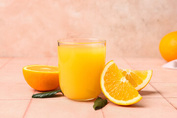 Glass of tasty juice with oranges and leaves on beige tile table