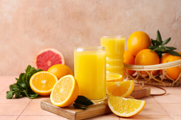 Wooden board with glass of tasty juice, oranges and leaves on beige tile table