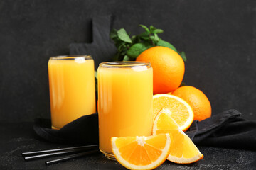 Glasses of tasty juice with oranges, mint leaves and straws on black grunge background