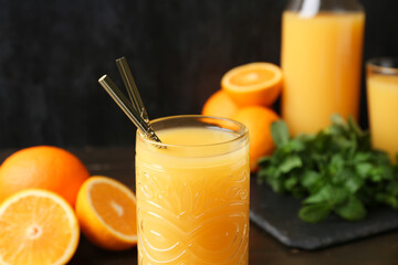 Glass of tasty orange juice with straws on black grunge background