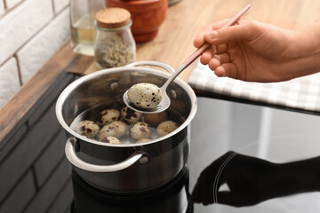 Woman holding spoon with boiled quail egg above cooking pot on electric stove