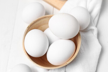 Bowl with raw chicken eggs on white wooden background