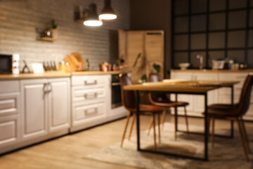 Blurred view of kitchen with counters, dining table and glowing lamps in evening