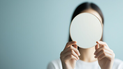 Person holding a round mirror in front of their face against a light blue background