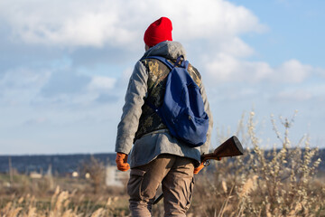 Mature hunter man holding a shotgun and walking through a field