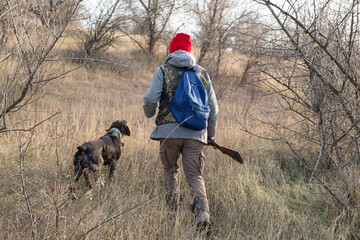 Mature hunter man holding a shotgun and walking through a field